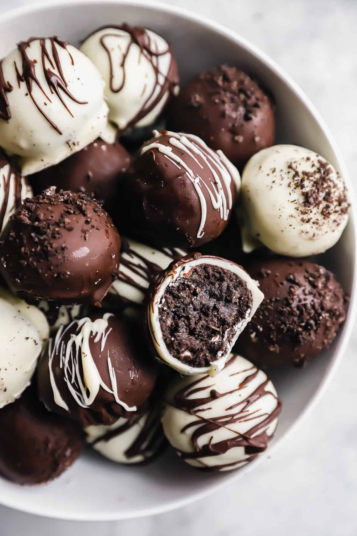 a bitten oreo ball resting on a pile of oreo balls in a white bowl.