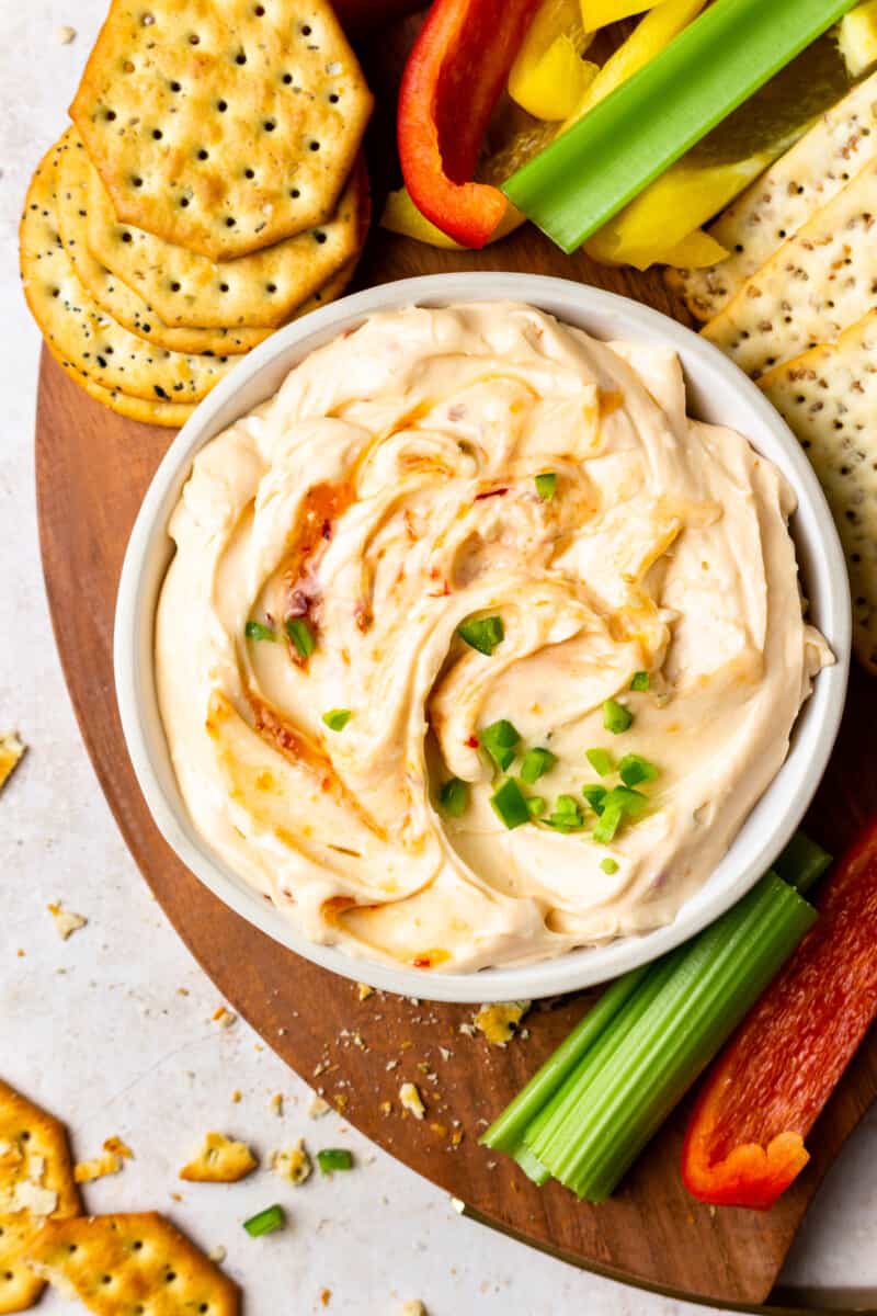 a bowl of hot pepper jelly dip on a board with crackers and veggie sticks