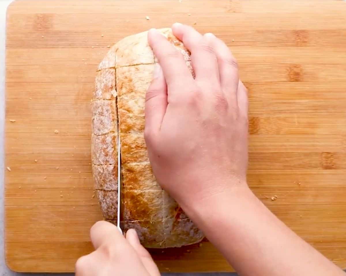 Slicing a crusty loaf of bread into a grid pattern on a cutting board to prepare pull-apart cheese bread.