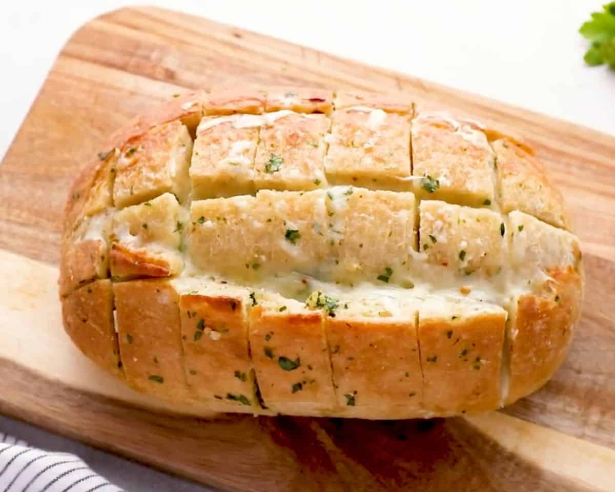 Pull apart cheese bread baked with garlic butter and melted cheese, sliced into a grid pattern on a wooden board.
