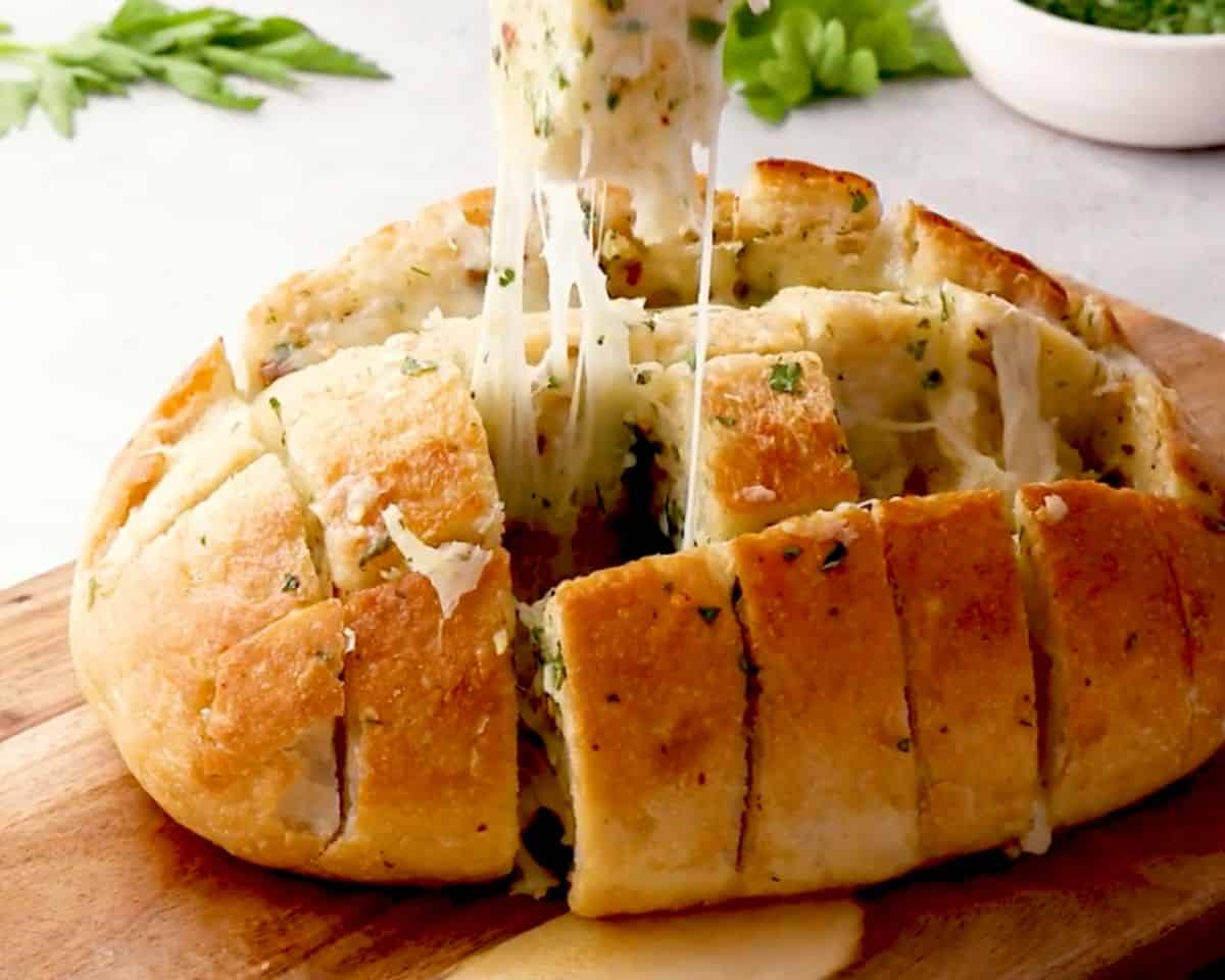 Close-up of pull apart cheese bread with melted cheese stretching as a piece is lifted from the loaf.