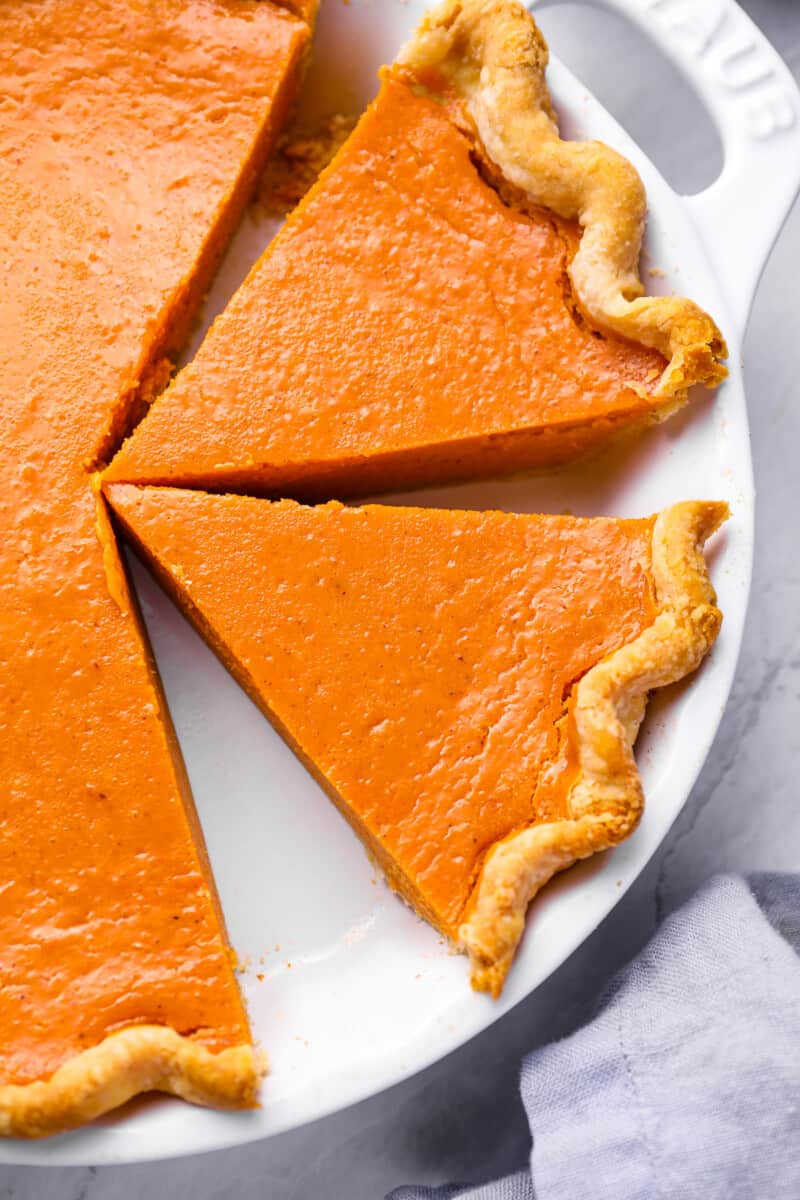 close up view of a partially sliced sweet potato pie in a white pie pan with handles.