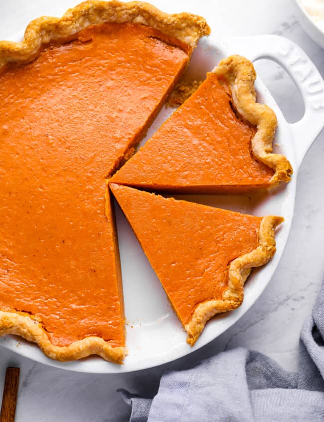 overhead view of a partially sliced sweet potato pie in a white pie pan with handles.