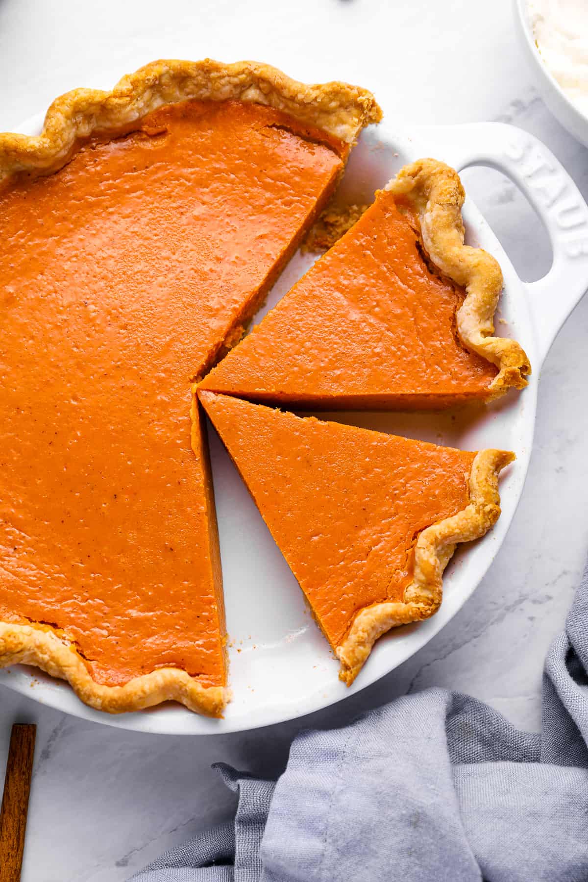 overhead view of a partially sliced sweet potato pie in a white pie pan with handles.