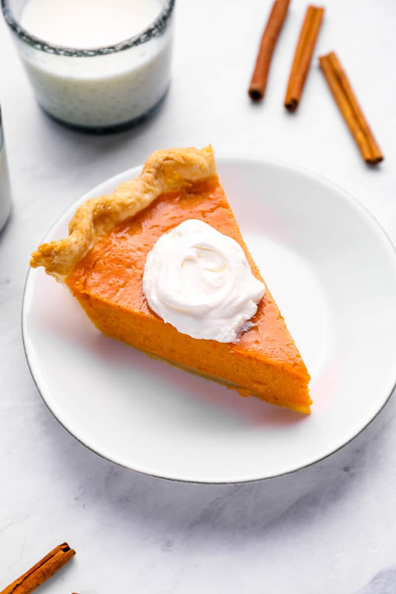 a slice of sweet potato pie on a white plate with a dollop of whipped cream.