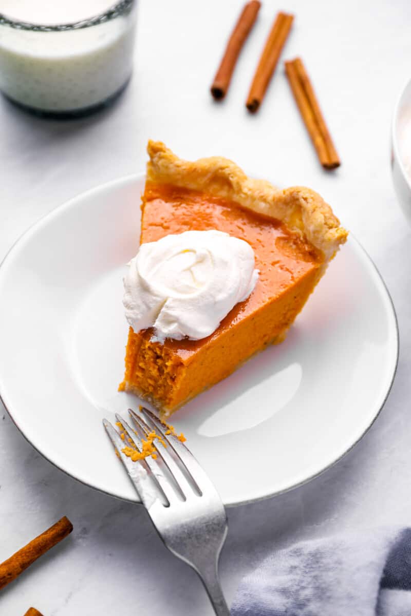 a partially eaten slice of sweet potato pie on a white plate with a fork and a dollop of whipped cream.