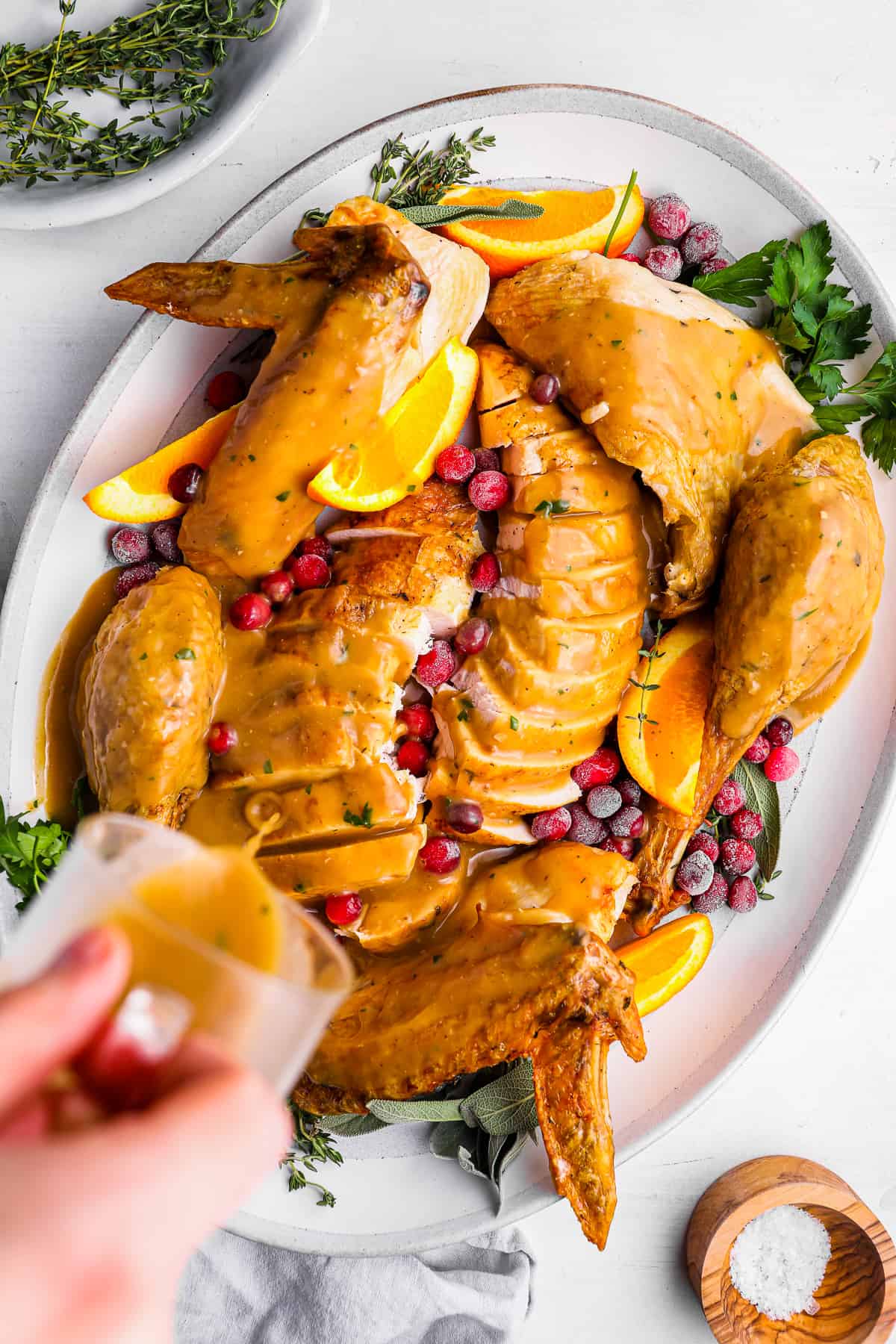 a hand pouring turkey gravy over a sliced whole turkey on a white plate.