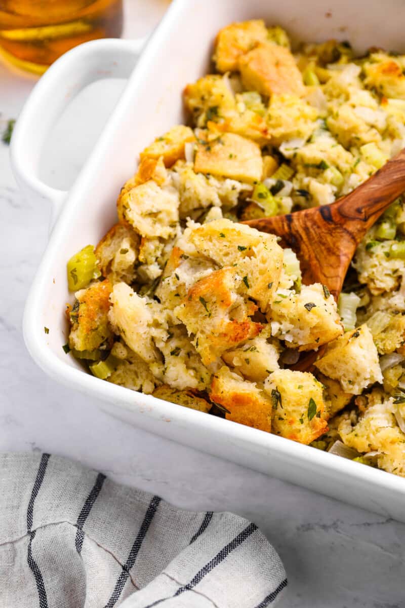 close up view of vegetarian stuffing in a white baking dish with a wooden spoon.