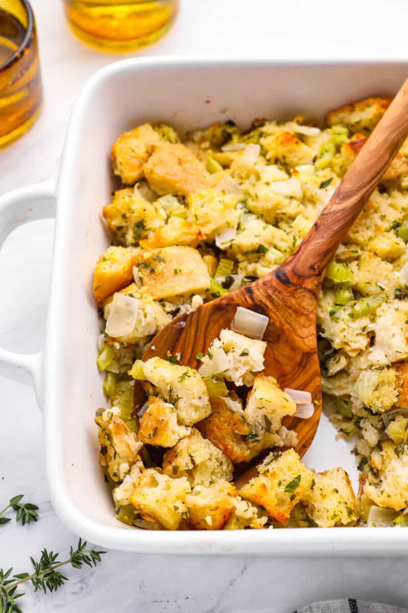 a spoon scooping vegetarian stuffing from a white baking dish.