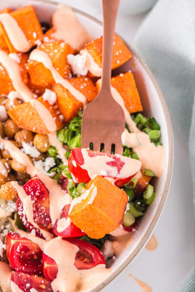 close up of a forkful of veggies hovering over a buddha bowl in a white bowl.