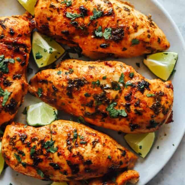 partial overhead view of 4 cilantro lime chicken breasts surrounded by lime wedges on a white plate.