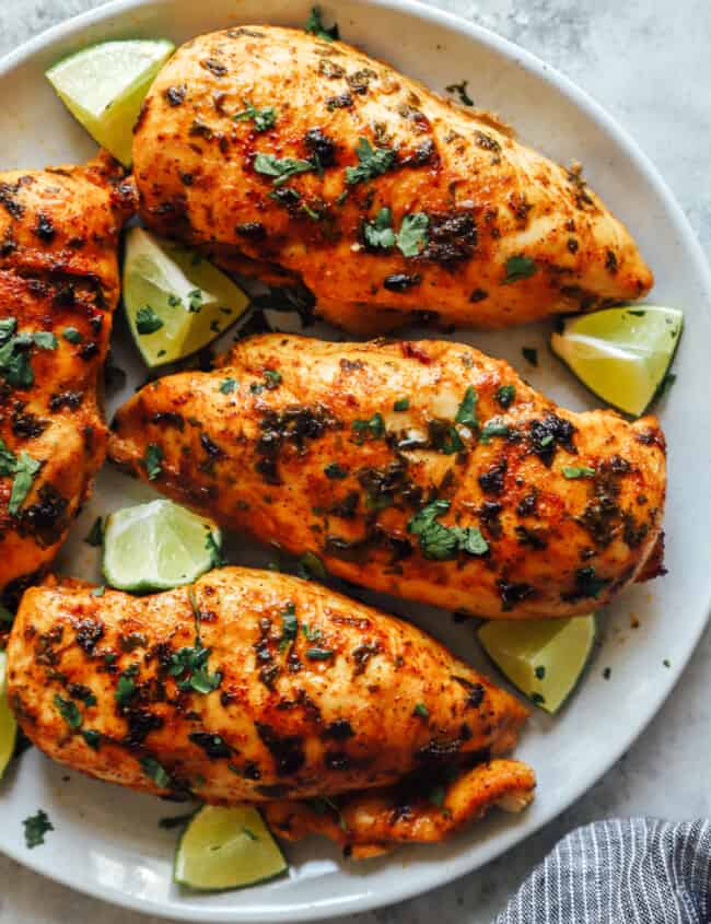 partial overhead view of 4 cilantro lime chicken breasts surrounded by lime wedges on a white plate.