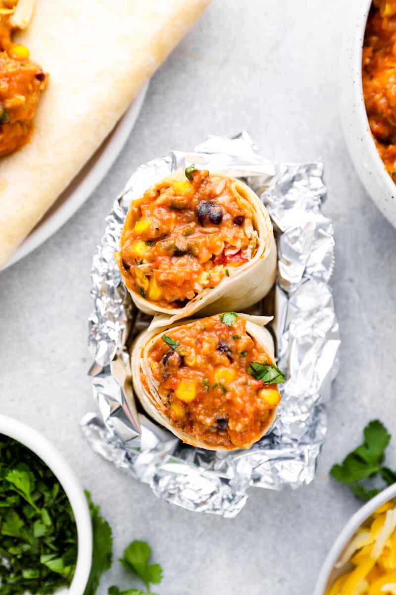 upturned crockpot chicken burrito halves wrapped in aluminum foil.