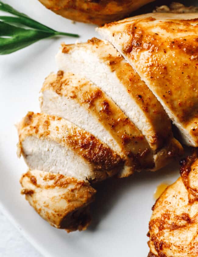 close up of a partially sliced baked marinated chicken breast on a white platter.