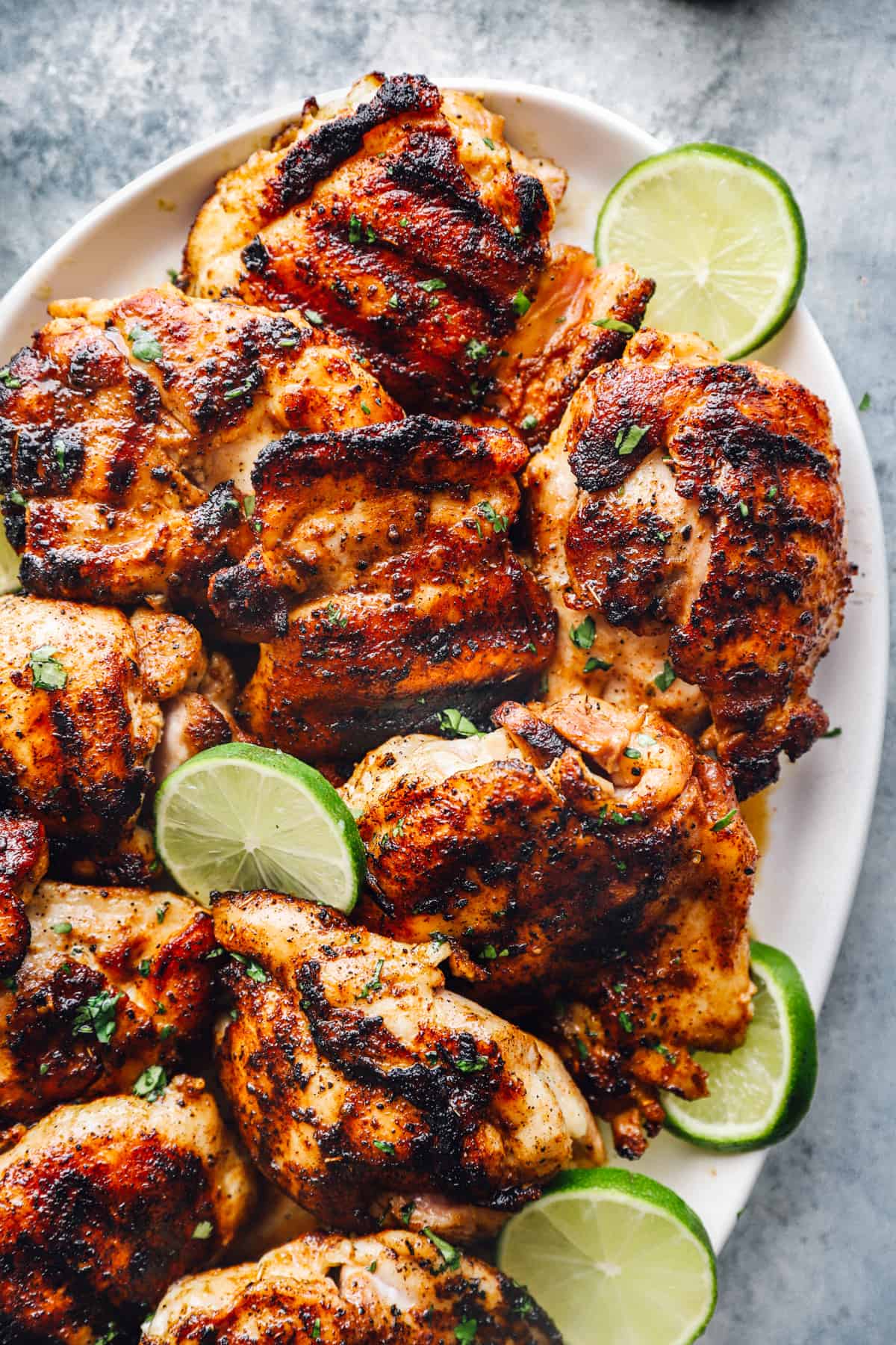 partial overhead view of grilled chicken thighs on a white oval serving platter with lime slices.