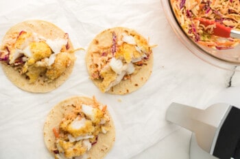 overhead view of 3 flat air fryer fish tacos with coleslaw and sauce on top.