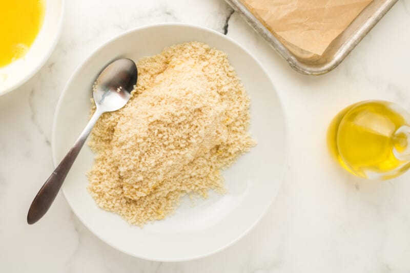 a piece of fish dipped in panko breadcrumbs on a white plate with a spoon.