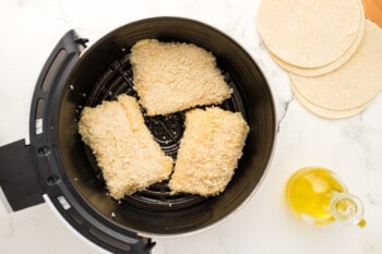 3 breaded raw fish filets in an air fryer basket.