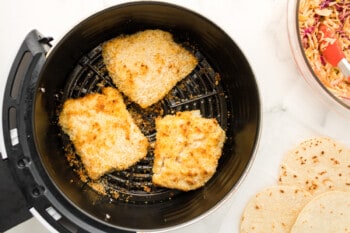 flipped breaded fish filets in an air fryer basket.