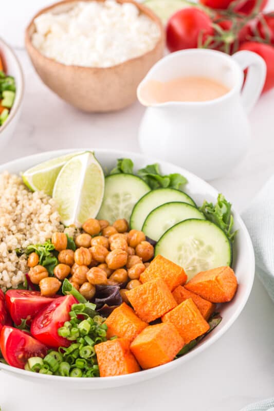 an assembled buddha bowl in a white bowl next to a carafe of dressing.