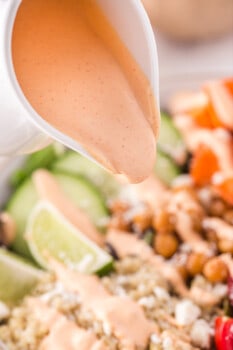 sriracha mayo dressing being poured over an assembled buddha bowl.