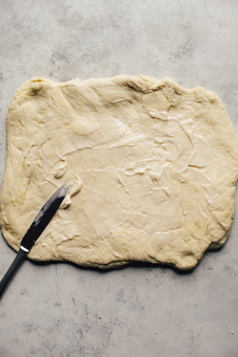 Butter being spread over Chicago deep dish pizza dough with a knife.