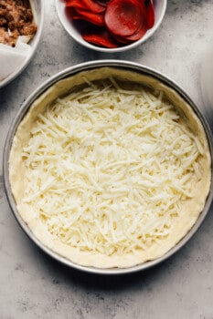 cheese sprinkled over chicago deep dish pizza crust in a baking pan.