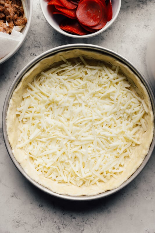 cheese sprinkled over chicago deep dish pizza crust in a baking pan.