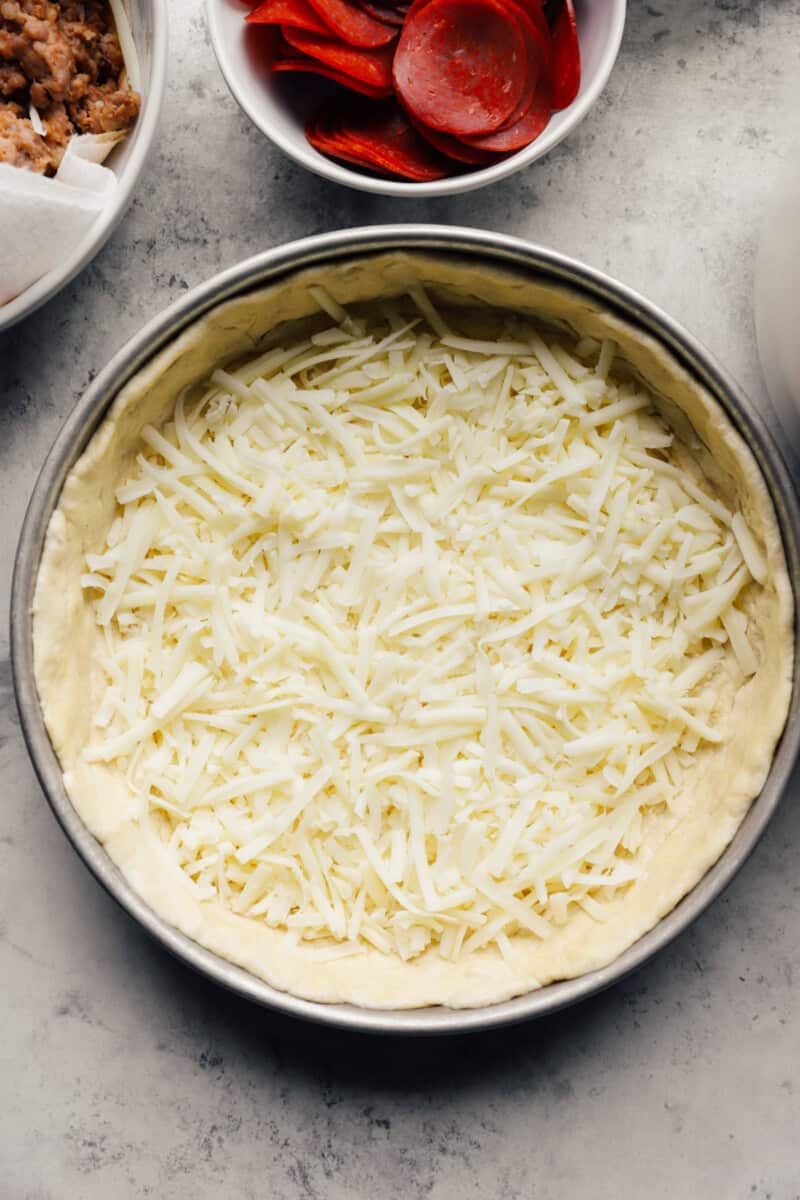Cheese sprinkled over chicago deep dish pizza crust in a baking pan.