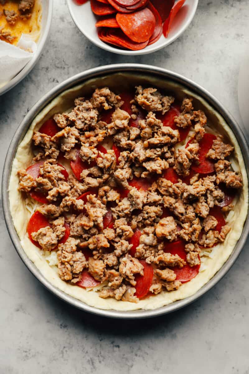 Sausage on top of pepperoni and cheese on a Chicago deep dish pizza pan.