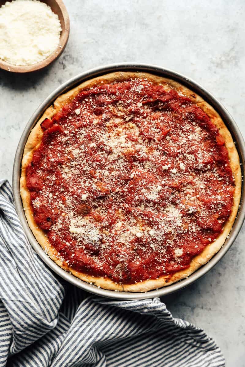 Sauce and Parmesan cheese over the toppings of a Chicago deep dish pizza in a baking pan.