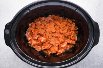taco seasoning sprinkled over cubed raw chicken in a crockpot.