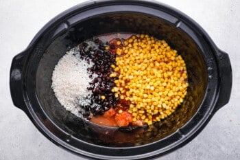 corn, beans, rice, and chicken broth poured over raw cubed chicken in a crockpot.