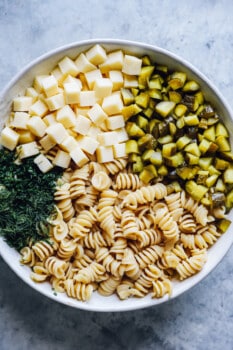 ingredients for dill pickle pasta salad in a white bowl.