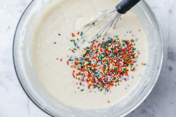 sprinkles added to funfetti cake batter in a glass bowl with a whisk.