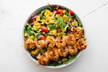 salad filled with veggies and topped with skewers of grilled shrimp