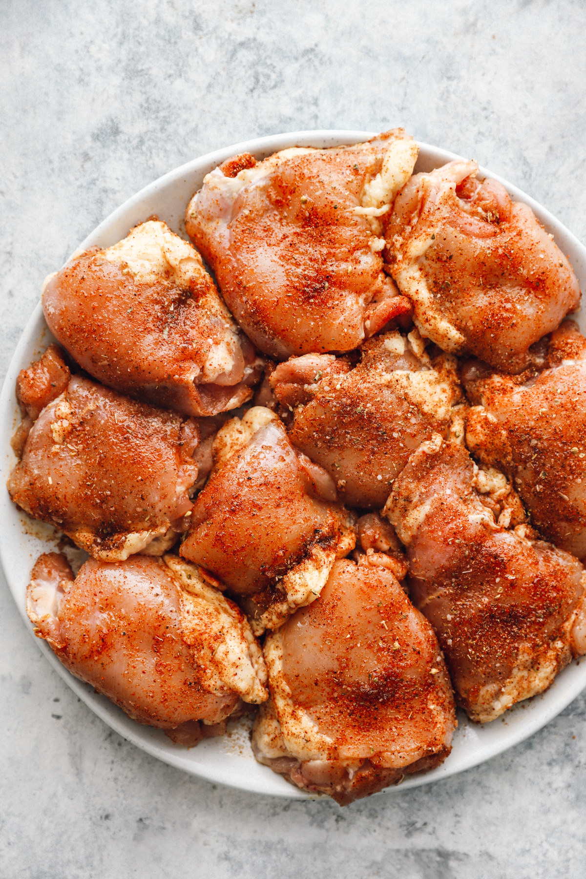 overhead view of seasoned raw chicken thighs on a white plate.