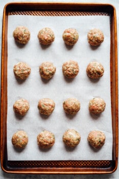 16 raw meatballs on a lined baking sheet.