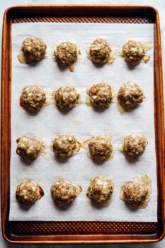 16 baked meatballs on a lined baking sheet.