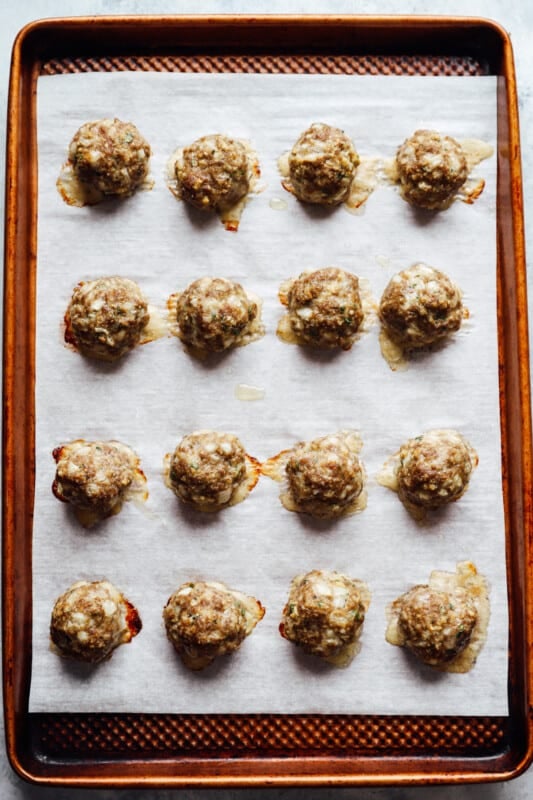 16 baked meatballs on a lined baking sheet.