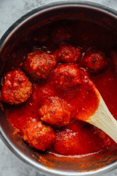 meatballs in marinara sauce in a saucepan with a wooden spoon.