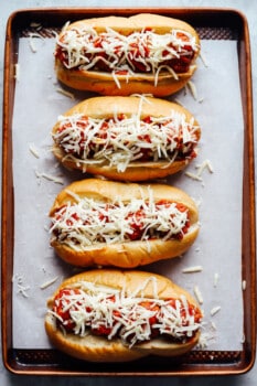 4 meatball subs topped with shredded cheese on a lined baking sheet.