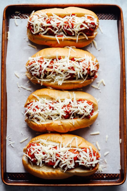 4 meatball subs topped with shredded cheese on a lined baking sheet.