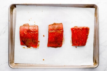 miso glaze brushed on 3 raw salmon filets on a lined baking sheet.