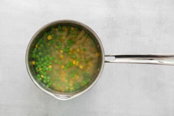 cooked pasta, peas, and corn in a saucepan.