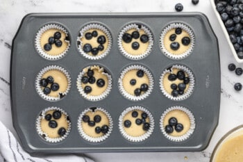 blueberry pancake muffin batter topped with blueberries in the wells of a muffin tin.