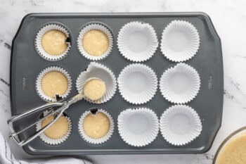 a cookie portion scoop spooning muffin batter into the lined wells of a muffin tin.