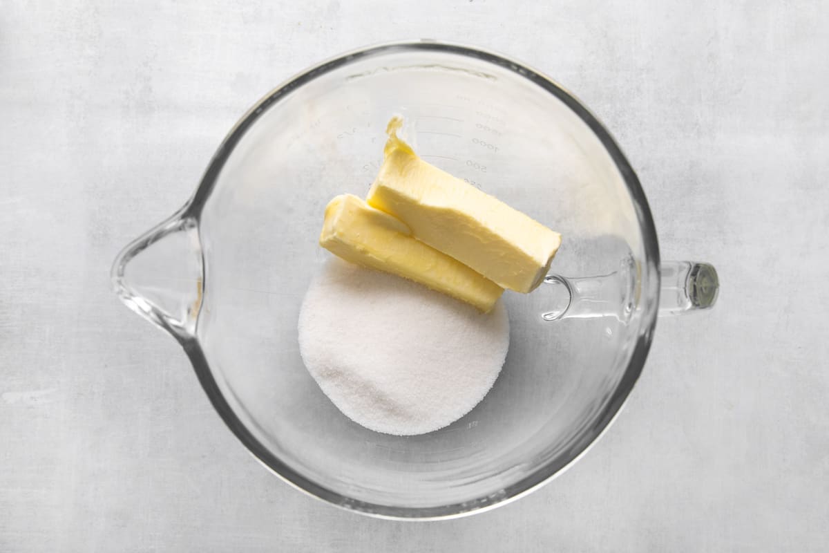 Sticks of butter and sugar in a mixing bowl.