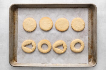 cookies lined up on a baking tray, four have Christmas shapes cut out of the middle