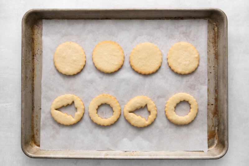 cookies lined up on a baking tray, four have Christmas shapes cut out of the middle